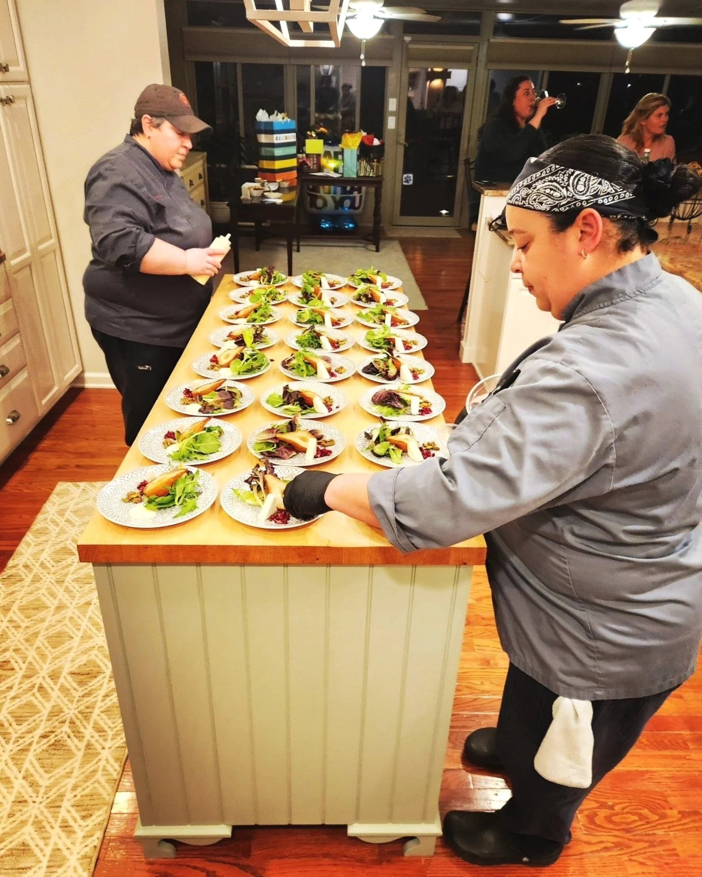 Two people preparing food on a counter with multiple plates of food.