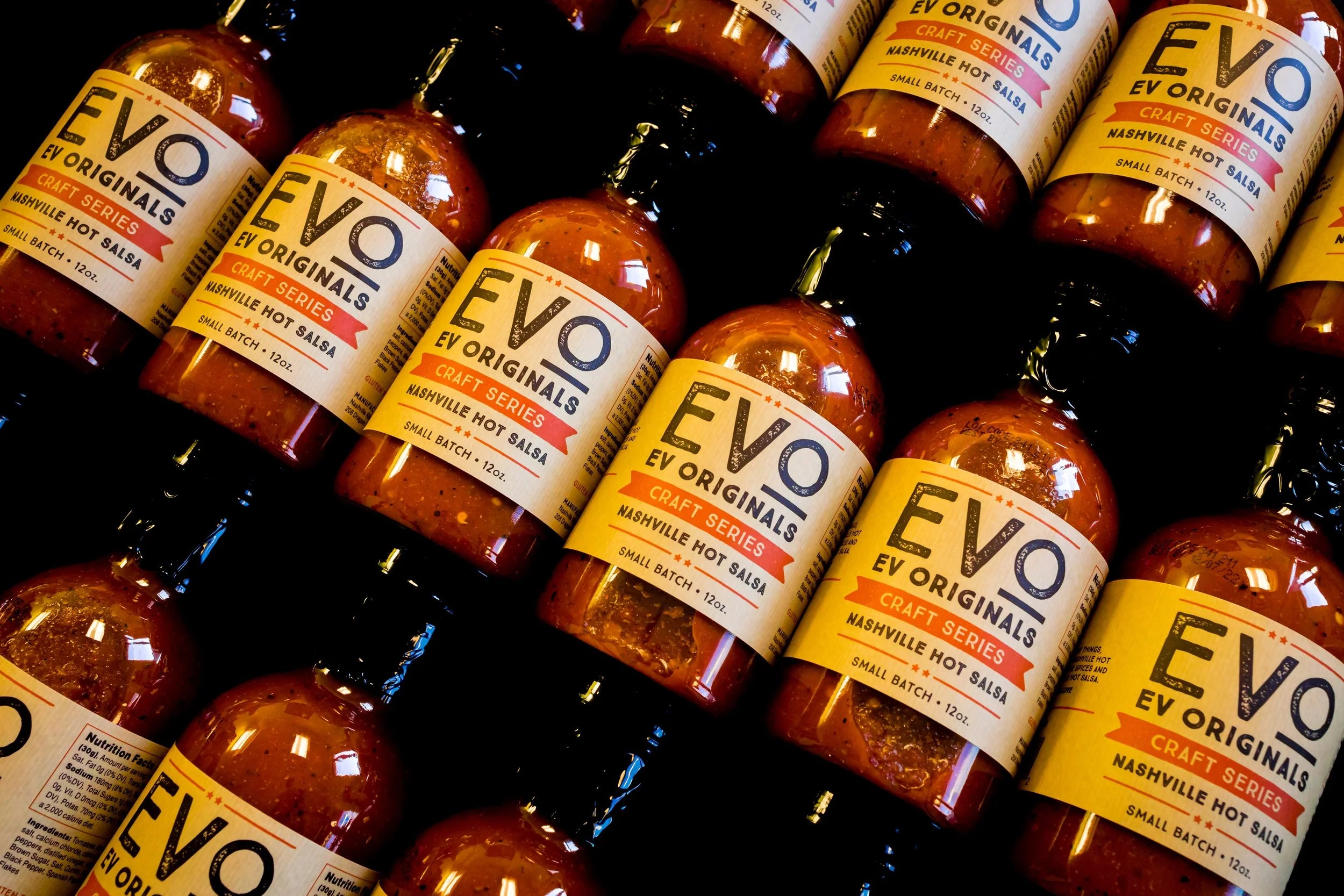 Multiple bottles of Evo Originals hot sauce with labels on a shelf.