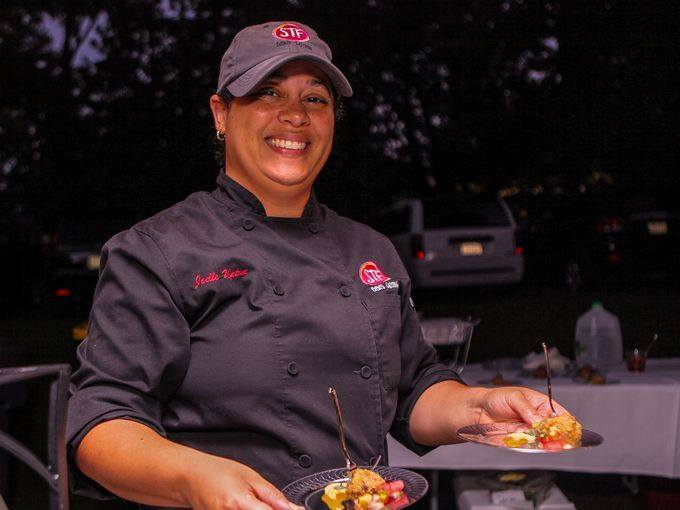 Person in a chef's uniform with a dish of food at night.